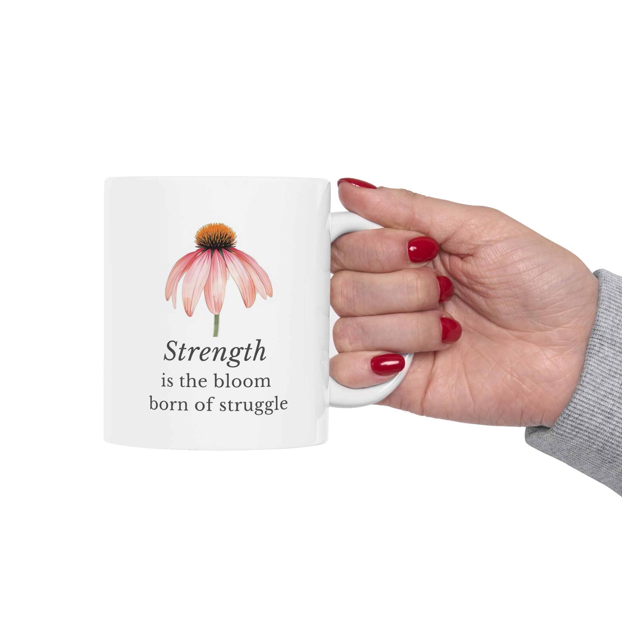 Hand holding a white ceramic mug with a echinacea design and motivational quote 'Strength is the bloom born of struggle' on a white background