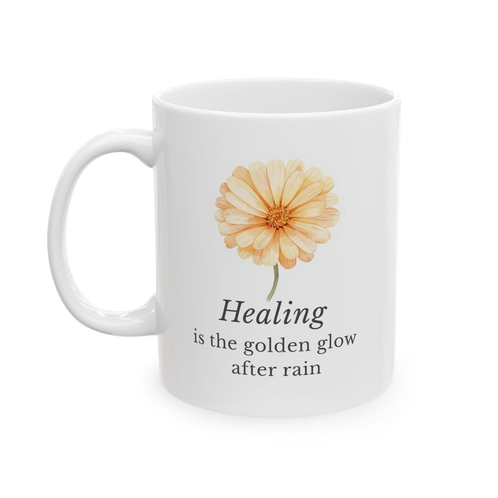 White ceramic mug with a calendula flower illustration and text 'Healing is the golden glow after rain' on a white background