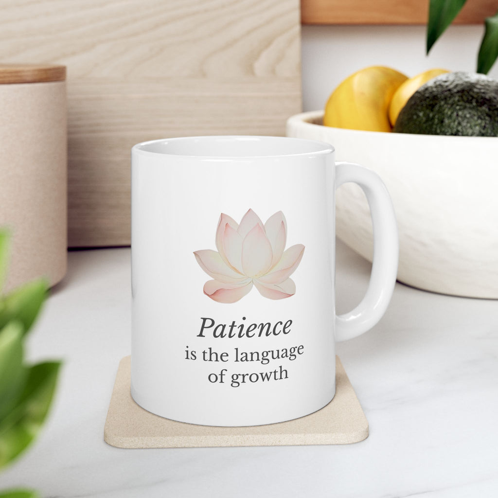 White ceramic mug with a pink lotus flower and 'Patience is the language of growth' text on a wooden coaster.
