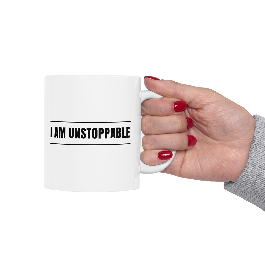 Hand holding a mug with 'I AM UNSTOPPABLE' text on a white background