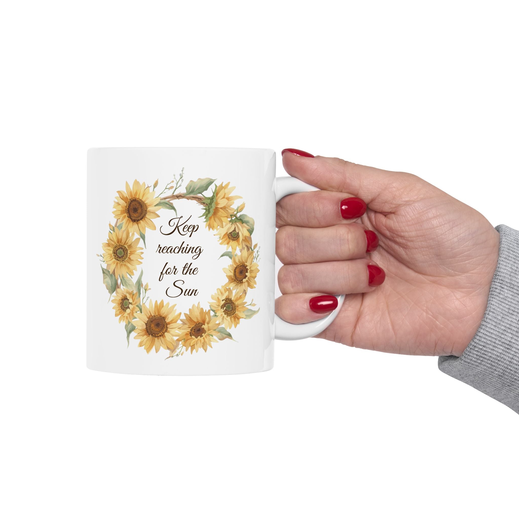 Mug with sunflower design and text held by a hand on a white background