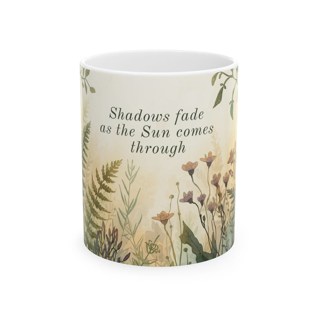 Ceramic mug with nature-themed design and text 'Shadows fade as the Sun comes through' on a white background