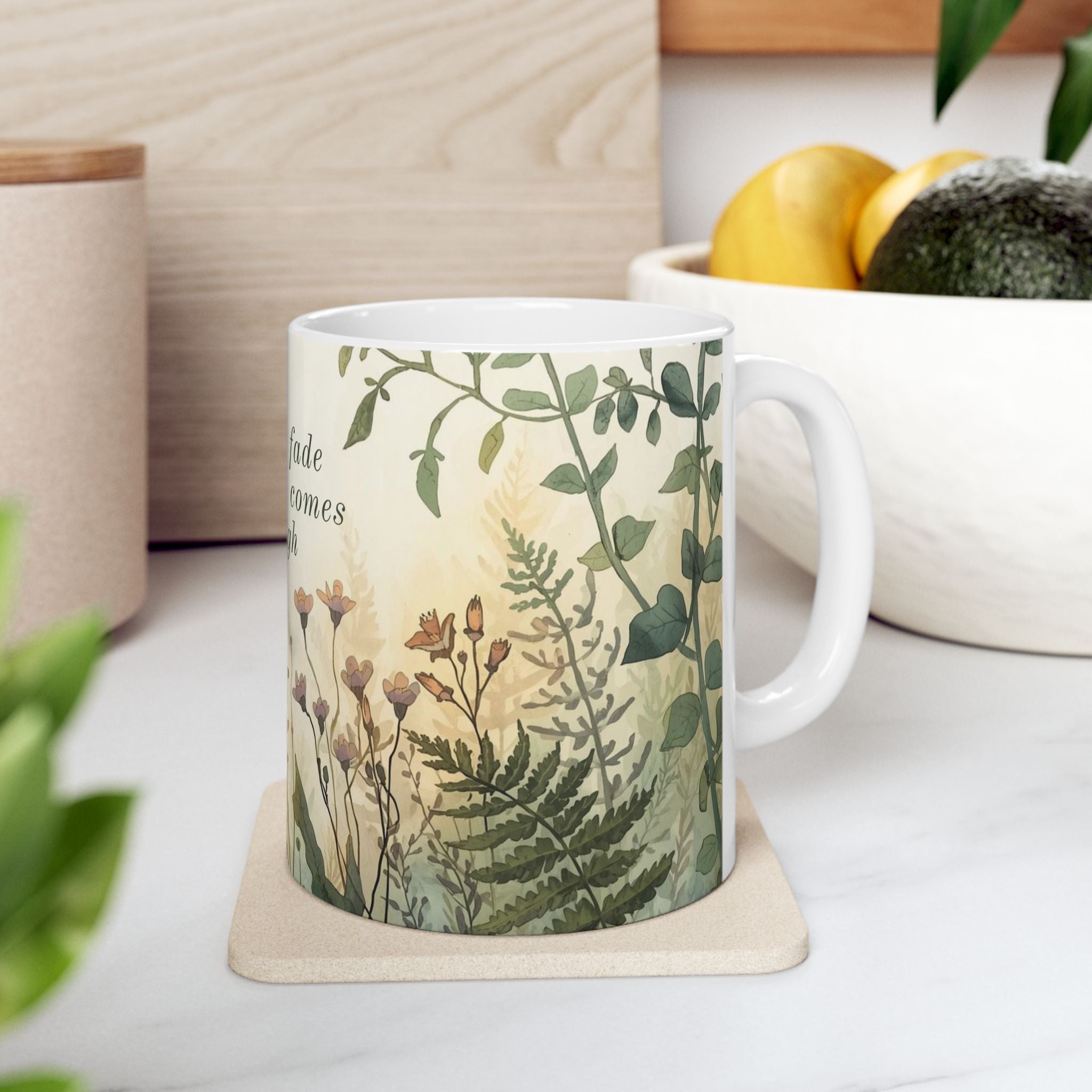 White ceramic mug with nature-themed design on a coaster, placed on a light surface with a plant and container in the background.