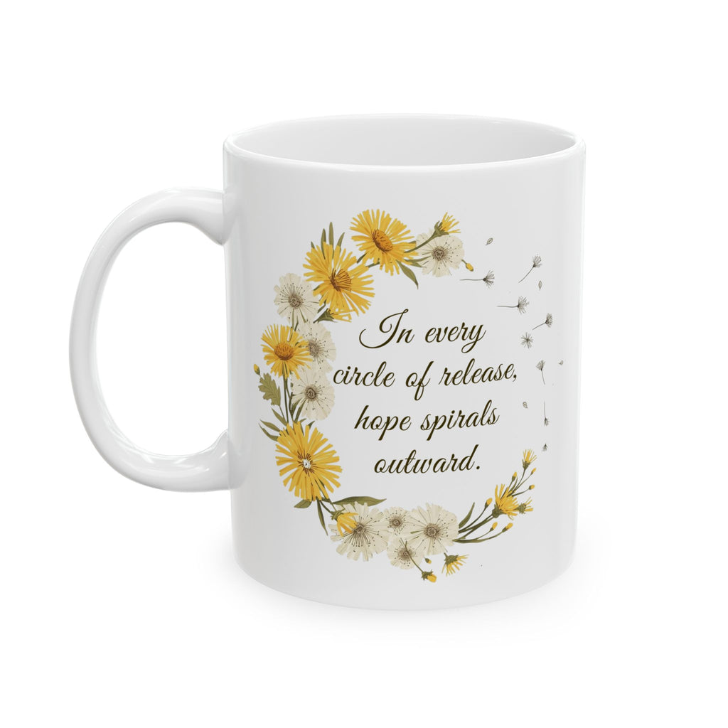 White ceramic mug with dandelion wreath design and text 'Inevery circle of release, hope spirals outward' on a white background