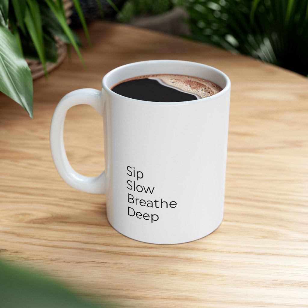 White mug with 'Sip Slow Breathe Deep' text on a wooden surface with coffee.