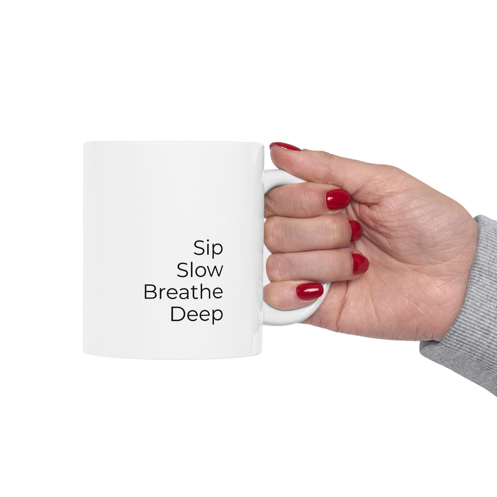 Hand holding a white mug with 'Sip Slow Breathe Deep' text on a white background